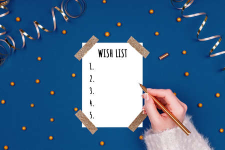 Woman writes New Year wish list. Flat lay image in gold and classic blue colors with isolated white card. Horizontalの写真素材