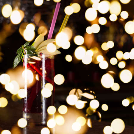 Cherry juice cocktail on the bar stand with dark background. Shallow DOF with festive bokeh lightsの写真素材