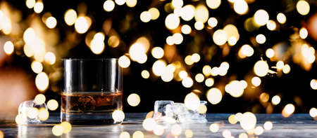 Glass of whiskey on the rocks with some ice on the table. Concept of hard liquor. Horizontal, wide screen banner format, isolated on black with festive holiday bokehの写真素材