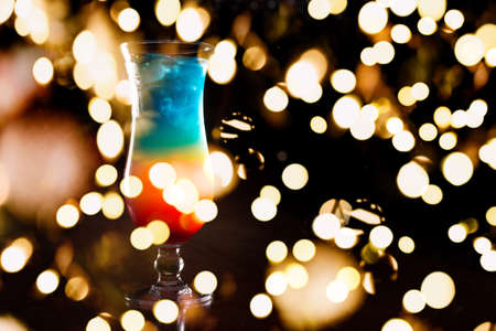 Rainbow cocktail on the bar stand with dark background. Shallow DOF with festive bokeh lightsの写真素材