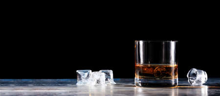 Glass of whiskey on the rocks with some ice on the table. Concept of hard liquor. Horizontal, wide screen banner format, isolated on blackの写真素材