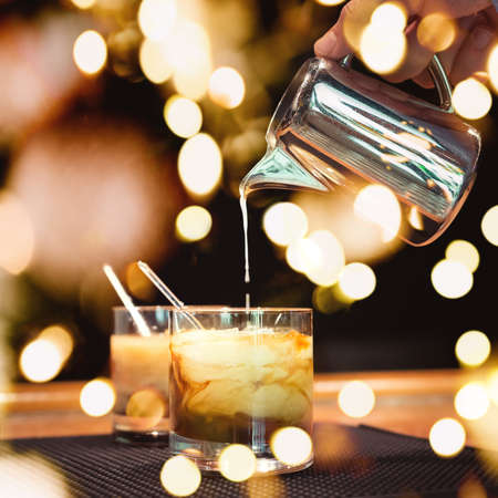 Preparation of white russian cocktails on the bar counter on rubber mat. Shallow DOF and marsala tonned with festive bokeh lightsの写真素材