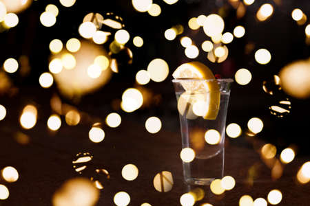 Tequila shot with lemon on the dark background. Shallow DOF with festive bokeh lights