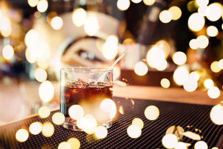 Black russian cocktail on the bar stand on rubber mat. Shallow DOF and marsala tonned with festive bokeh lightsの写真素材