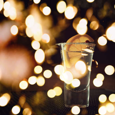 Tequila shot with lemon on the dark background. Shallow DOF with festive bokeh lightsの写真素材