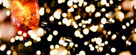 Tasty alcoholic trendy cocktail with orange slice on black background. Macro, wide screen banner format with festive holiday bokehの写真素材