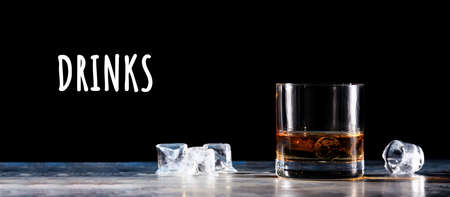 Glass of whiskey on the rocks with some ice on the table. Concept of hard liquor. Horizontal, wide screen banner format, isolated on black with Drinks wordingの写真素材