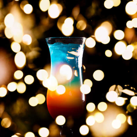 Rainbow cocktail on the bar stand with dark background. Shallow DOF with festive bokeh lightsの写真素材