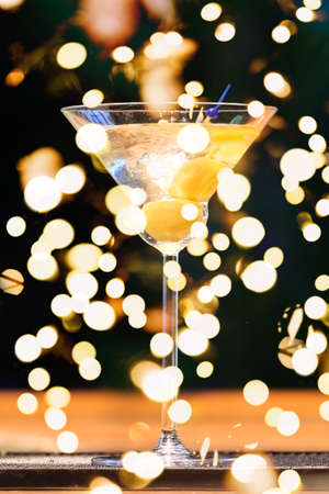 Martini at the bar counter. Classic cocktail in the bar. Dark background. Focus on the liquid. Vertical, macro view with festive holiday bokehの写真素材
