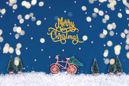 Funny cozy scene with Christmas toys on classic blue with bokeh lights. Christmas tree is moved home by bicycle on the snow road. Horizontalの写真素材