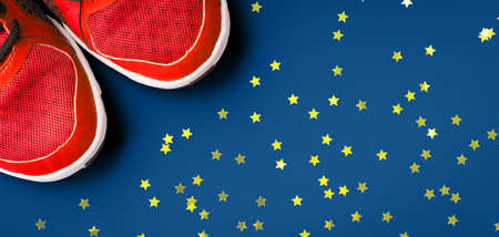 Sneakers on the solid classic blue backdrop. Keep fit athletic and healthy sports concept. Banner format, top view with festive golden star shaped confettiの写真素材