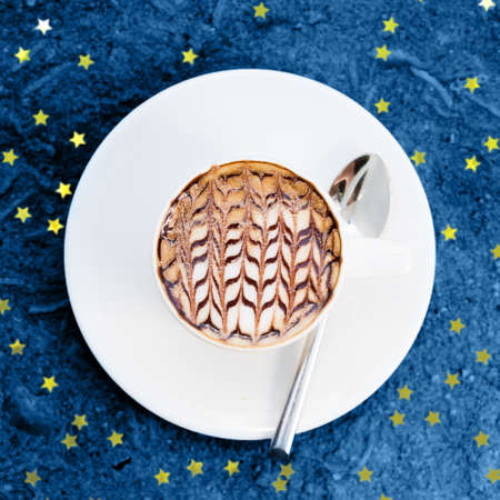 Overhead view of cafe latte with craft design on it toned in blue. Square with festive golden star shaped confettiの写真素材