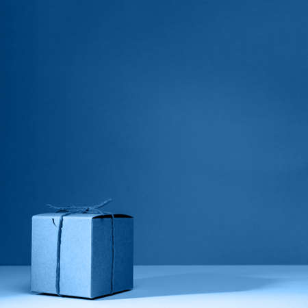 Craft cardboard gift box on the solid classic blue background. Holiday and gift concept. Squareの写真素材