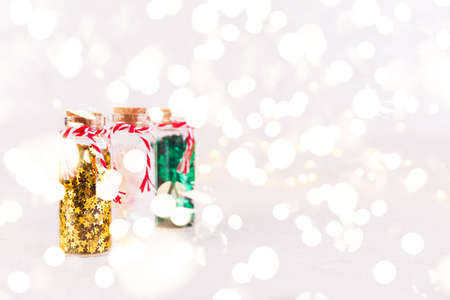 Glass bottles with glitter confetti on white background with bokeh lights. Holiday Christmas and New Year background. Horizontal with festive bokeh lightsの写真素材