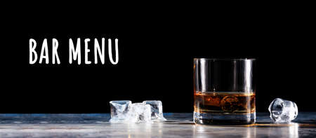 Glass of whiskey on the rocks with some ice on the table. Concept of hard liquor. Horizontal, wide screen banner format, isolated on black with Bar menu wordingの写真素材
