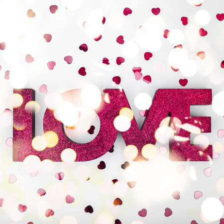 Dark red sign LOVE and glitter heart confetti. Valentine day concept. Trendy minimalistic flat lay design background. Square with festive bokeh lightsの写真素材