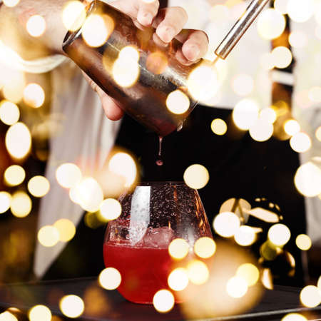 Barman in making cocktail at a nightclub. Nightlife concept. No face. Pouring into glass. Square with festive bokeh lightsの写真素材