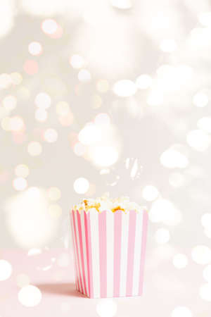 Popcorn bag with white and pink stripes at the festive lights bokeh backdrop. Empty minimalistic background. Romantic movie night and snack concept. Verticalの写真素材