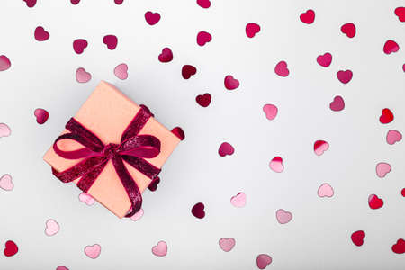Craft box with dark red velvet ribbon bow and glitter heart confetti. Valentine day and eco-friendly wrapping concept. Trendy minimalistic flat lay design background. Horizontalの写真素材