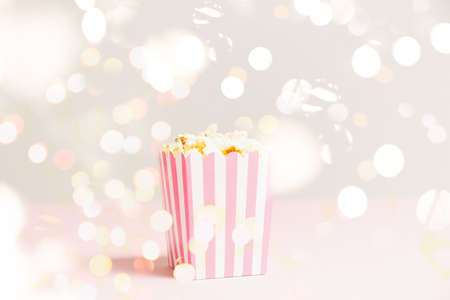 Popcorn bag with white and pink stripes at the festive lights bokeh backdrop. Empty minimalistic background. Romantic movie night and snack concept. Horizontalの写真素材
