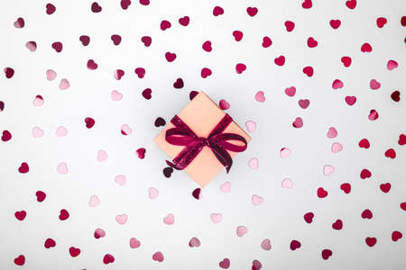 Craft box with dark red velvet ribbon bow and glitter heart confetti. Valentine day and eco-friendly wrapping concept. Trendy minimalistic flat lay design background. Horizontalの写真素材
