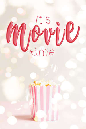 Popcorn bag with white and pink stripes at the festive lights bokeh backdrop. Empty minimalistic background. Romantic movie night and snack concept with Its movie time wording. Verticalの写真素材