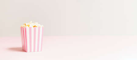 Popcorn bag with white and pink stripes at the light neutral backdrop. Empty minimalistic background. Romantic movie night and snack concept. Banner wide screen formatの写真素材