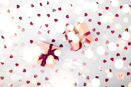 Craft box with dark red velvet ribbon bow and glitter heart confetti. Valentine day, eco-friendly wrapping concept. Trendy minimalistic flat lay design background. Horizontal with festive bokeh lightsの写真素材