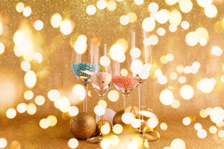 Glasses with sprinkles and toys on the festive golden background. Christmas and New Year party concept. Stylish trendy holiday season. Horizontal with festive bokeh lightsの写真素材
