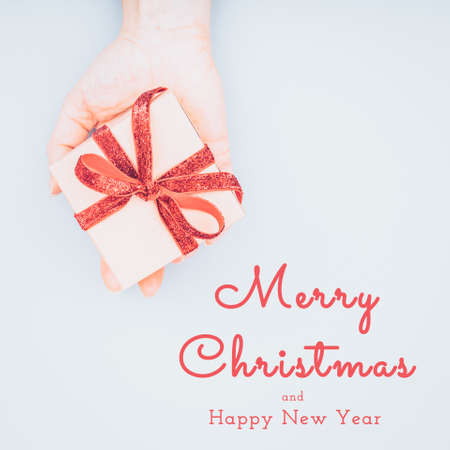 Craft box with red ribbon bow in female hand. Valentine day concept. Trendy minimalistic flat lay design background in light cold toning. Square with Seasonal greetingsの写真素材