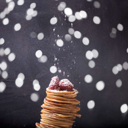 Stack of pancakes with raspberries on top. Homemade dessert. Maslenitsa concept. Dark grey background. Sifting powder sugar. Square and some bokehの写真素材
