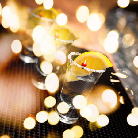 Three tequila shots with lemon on a bar ribber mat. Shallow DOF and toned with festive bokeh lightsの写真素材
