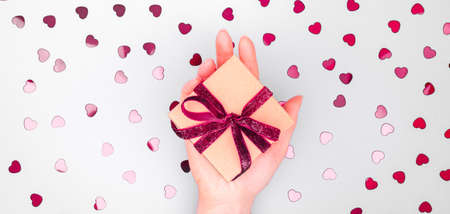 Craft box with dark red velvet ribbon bow in female hand. Valentine day and eco-friendly wrapping concept. Trendy minimalistic flat lay design background. Wide screen banner formatの写真素材