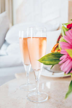 Two glasses of rose champagne in the upscale hotel room. Dating, romance, honeymoon, valentine, getaway concepts. Vertical. Light blue toningの写真素材
