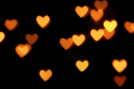 Black background with bright warm heart shaped bokeh lights. Holiday, Valentines Day background. Ideal to layer with any design. Horizontalの写真素材