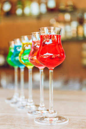 Many colorful tasty creative alcoholic cocktails in a row on bar stand. Luxury vacation concept.