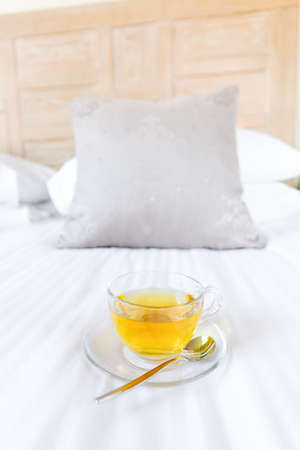 Herbal tea on bed linen in the upscale hotel room. Being alone, getaway, staycation, digital detox concepts. Verticalの写真素材