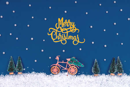 Funny cozy scene with Christmas toys on classic blue. Christmas tree is moved home by bicycle on the snow road. Horizontalの写真素材