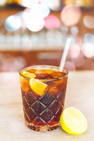 Glass of tasty alcoholic Black Russian cocktail with vodka and coffee liquor with lemon slice and straw on bar stand. Party concept. with festive bokeh lights effectの写真素材
