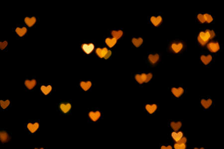 Black background with bright warm heart shaped bokeh lights. Holiday, Valentines Day background. Ideal to layer with any design. Horizontalの写真素材