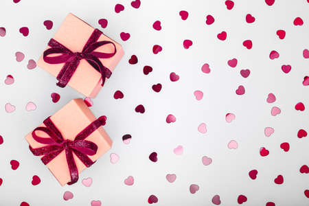 Craft box with dark red velvet ribbon bow and glitter heart confetti. Valentine day and eco-friendly wrapping concept. Trendy minimalistic flat lay design background. Horizontalの写真素材