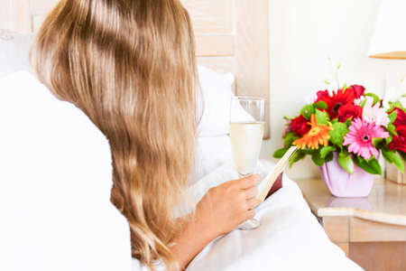 Girl relaxing in her hotel room with a glass of sparkling drink and a book. Vacation, relaxation, self time, romance and getaway concepts. Horizontalの写真素材