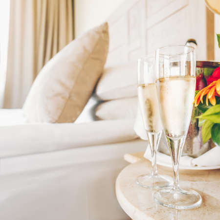Two glasses of champagne in the upscale hotel room. Dating, romance, honeymoon, valentine, getaway concepts. Square. Light warm toningの写真素材