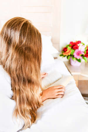 Girl relaxing in her hotel room: reading a book. Vacation, relaxation, self time and getaway concepts. Verticalの写真素材