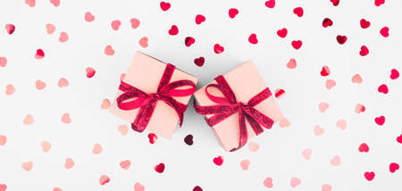 Craft box with red ribbon bow and glitter heart confetti. Valentine day and eco-friendly wrapping concept. Trendy minimalistic flat lay design background. Wide screen banner formatの写真素材