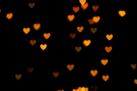 Black background with bright warm heart shaped bokeh lights. Holiday, Valentines Day background. Ideal to layer with any design. Horizontalの写真素材