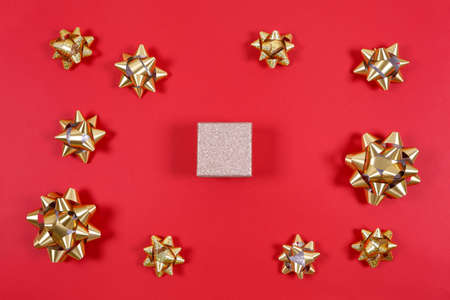 Gift box with recycled materials bow and golden gift bows on the red background with place for text. Traditional celebration and gift giving concept, eco friendly packagingの写真素材