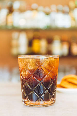 Glass of tasty alcoholic Black Russian cocktail with vodka and coffee liquor over blurred background on bar stand. Vacation concept.の写真素材