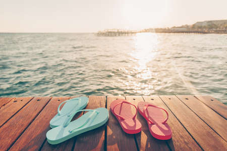 Two pairs of flip flops at the wooden pier during sunset. Luxury vacation resort. Holiday getaway concept. Horizontal, warm toningの写真素材