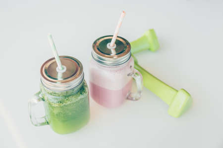 Healthy smoothie options in eco friendly glass jars with paper straws and light dumbbels in a luxury gym recreation area or vegan cafe. Trendy muted toning, place for textの写真素材